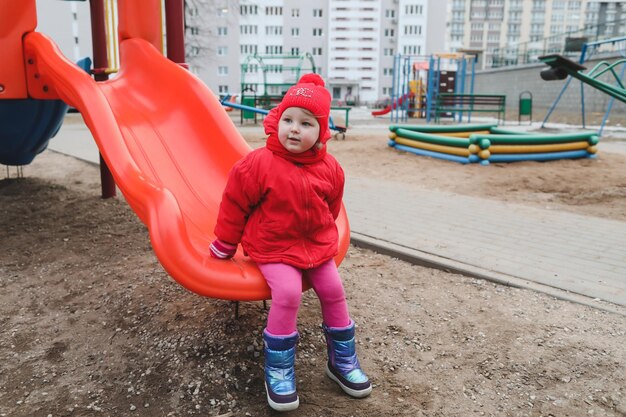 Chica feliz en una chaqueta roja cabalga sobre una colina en el patio de recreo divertida niña alegre jugando