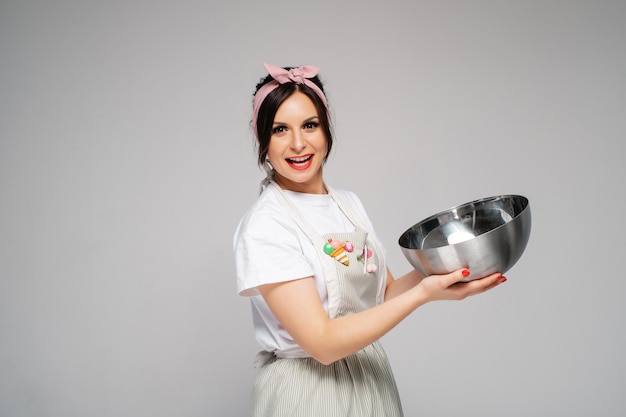 Chica feliz cocinero pastelero en un delantal sostiene un tazón