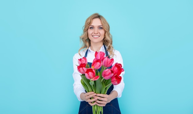 Chica feliz en delantal con flores de tulipán de primavera sobre fondo azul.