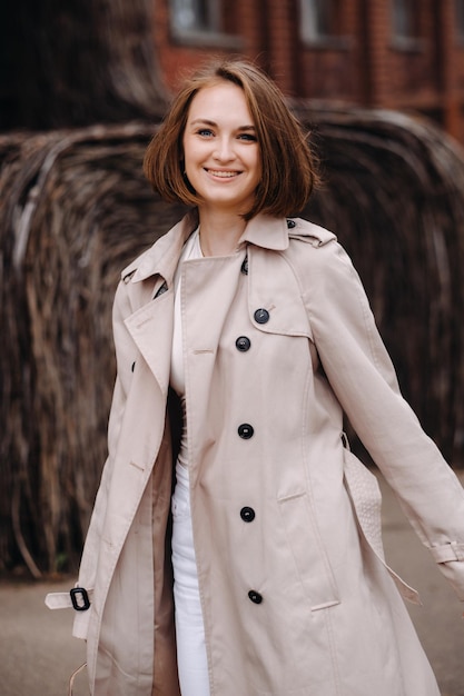 Una chica feliz y elegante con un abrigo gris camina por la ciudad