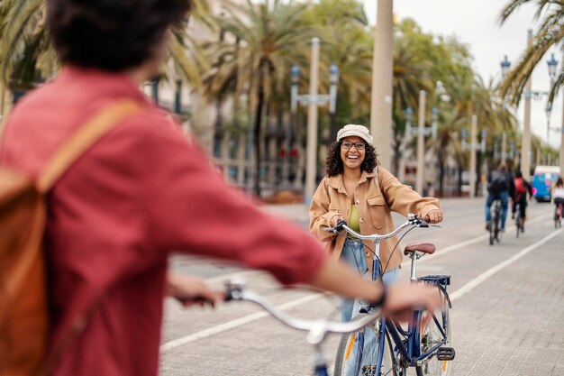 Una chica feliz está caminando hacia su amiga y sonriéndole. Ambos están empujando bicicletas.