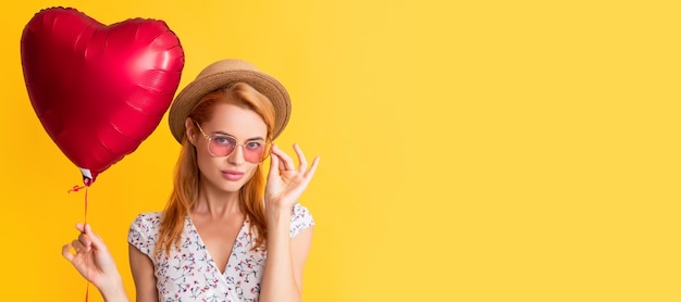 Chica feliz en gafas de sol sostiene globo de corazón de amor sobre fondo amarillo Banner de retrato de cara aislada de mujer con espacio de copia