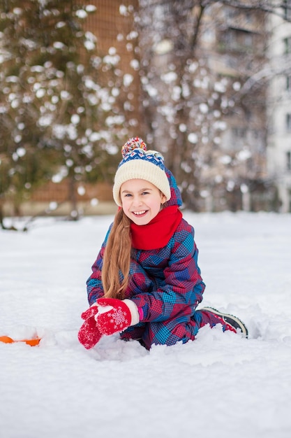 Chica feliz jugando con nieve en un paseo de invierno cubierto de nieve haciendo bolas de nieve en el parque