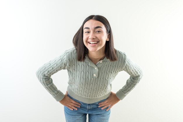 Chica feliz con las manos en las caderas se siente feliz y tiene una bonita sonrisa suéter verde y vaqueros