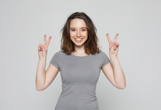 Chica feliz mirando a la cámara con una sonrisa y mostrando el signo de la paz con los dedos