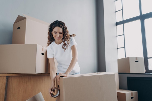 Chica feliz se mueve sola Mujer joven está empacando cajas con cinta adhesiva para el envío