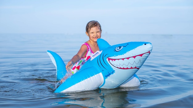 Foto chica feliz nadando en un juguete de tiburón inflable en el mar