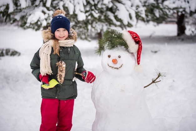 Chica feliz niño lindo rubio plaing con un muñeco de nieve