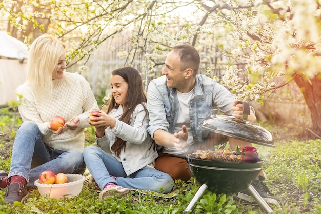 Chica feliz, padre y madre preparando barbacoa en el patio.