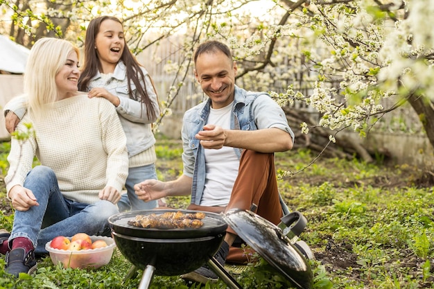 Chica feliz, padre y madre preparando barbacoa en el patio.