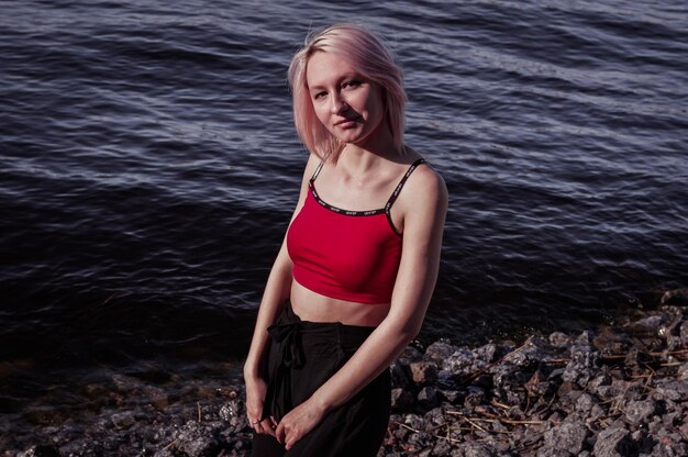 Foto chica feliz con el pelo corto y un top rojo en la orilla del mar