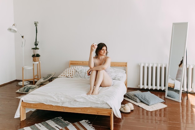 Una chica feliz en pijama bebiendo café mira el teléfono usando tecnología mientras está acostada en la cama en casa