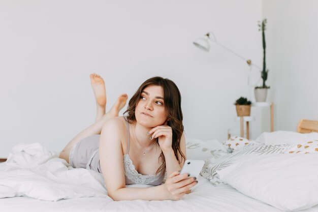 Una chica feliz en pijama se toma una selfie se comunica usando su teléfono y tecnología en la cama en casa.