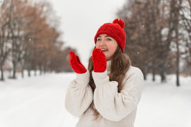 Chica feliz riendo con sombrero rojo y mitones en el parque de invierno Hermosa joven caminando en invierno