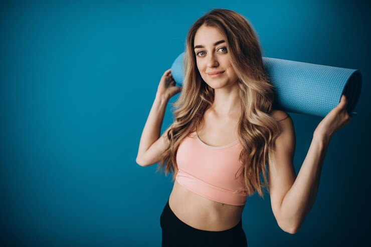 Chica feliz en ropa deportiva posando con estera de yoga en estudio
