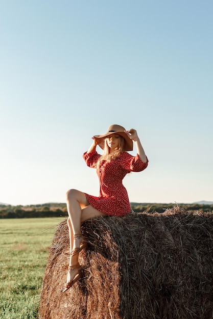 Chica feliz sentada en un puñado de heno en un campo de verano al atardecer