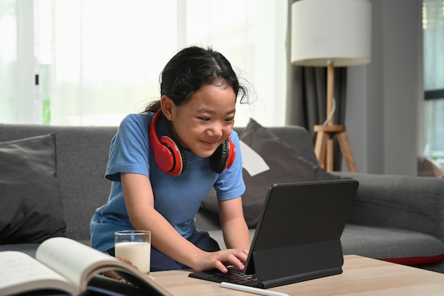 Chica feliz sentada en el sofá y viendo dibujos animados en línea con tableta digital en casa