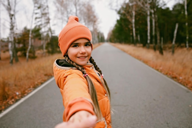 Chica feliz con sombrero naranja invita a compartir con su placer de caminar por el bosque de otoño