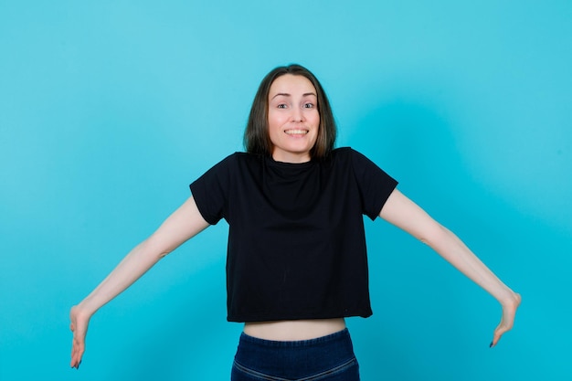 Foto la chica feliz sonríe abriendo los brazos de par en par con el fondo azul