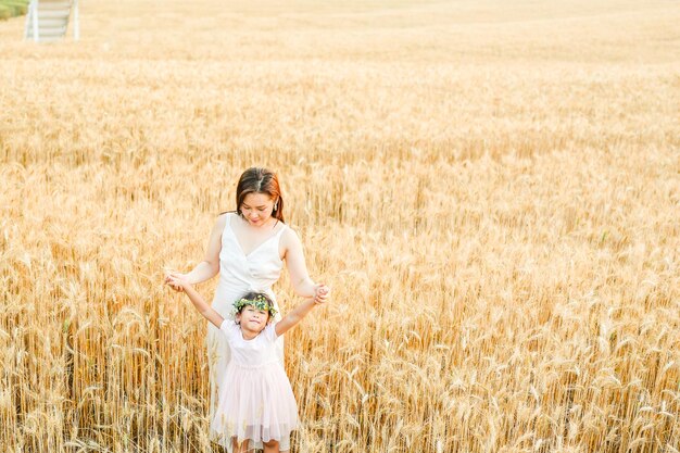 Chica feliz con su madre de pie en el campo de trigo