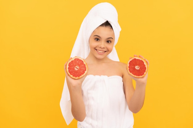 Chica feliz en toalla con pomelo sobre fondo amarillo