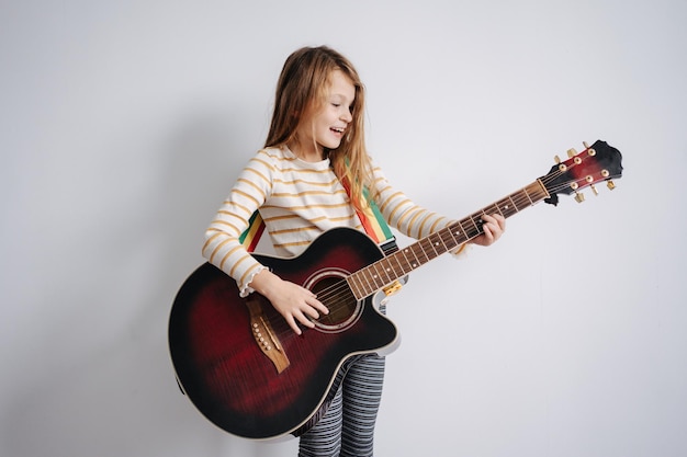 Chica feliz tocando la guitarra de tamaño completo usando ropa de dormir frente a una pared en blanco