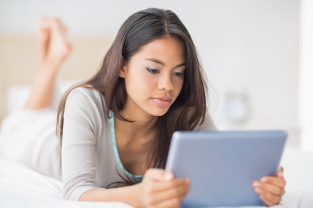 Chica feliz tumbado en la cama con su tablet pc