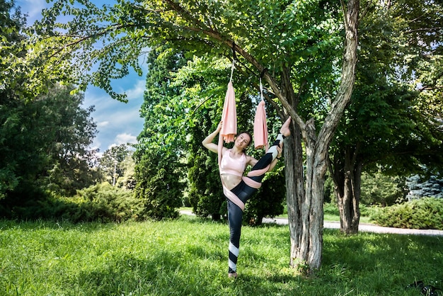 Chica con una figura bombeada en un traje deportivo para estiramientos de yoga en el aire cerca de un árbol