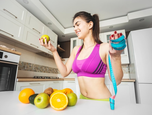 Chica fitness cerca de la mesa de la cocina con fruta y medidor para mantenerse en forma con el concepto de dieta saludable