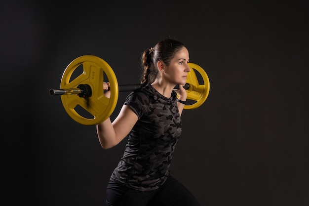 Chica fitness en una plataforma escalonada con una barra de tortitas amarillas en un estante Ir a hacer deporte en