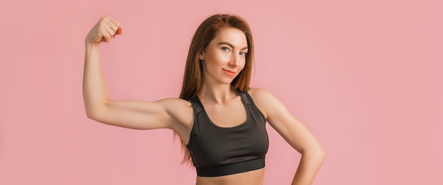 Chica fitness sonriendo en ropa deportiva negra sobre una pared rosa