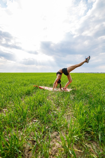 Chica flexible, acróbata, puente de gimnasia, parada de manos, mujer elegante. En la naturaleza, realiza hermosas poses de flexibilidad, un modelo deportivo sobre un fondo de cielo azul.