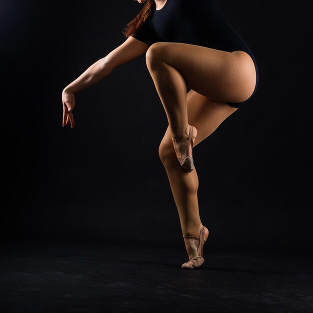 Chica flexible artista de gimnasia rítmica saltando sobre fondo blanco oscuro gracia en acción de movimiento