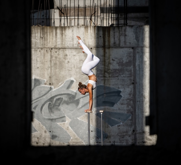 Foto chica flexible y en forma de pie sobre sus manos manteniendo el equilibrio en el edificio abandonado