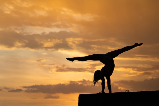 Chica flexible haciendo ejercicio en el fondo del cielo durante la espectacular puesta de sol