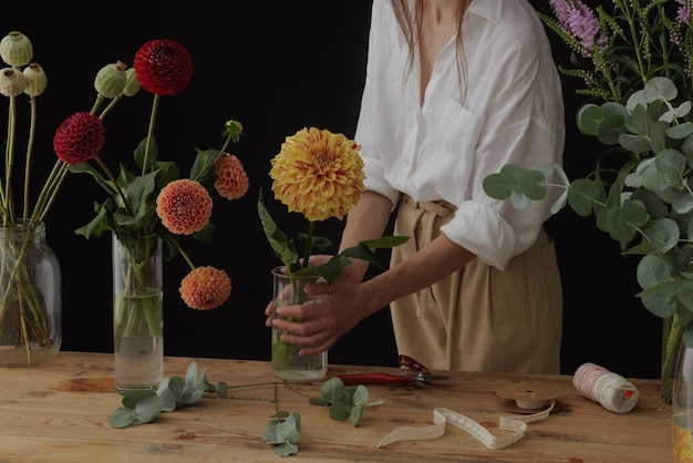 Chica florista recoge un ramo en un taller de flores en un diseño de fondo oscuro para la floristería