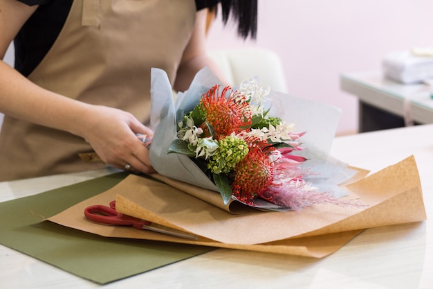 Chica de floristería en delantal de arena en el trabajo crea un ramo de proteas