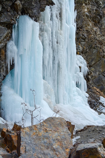 Una chica en el fondo de una cascada congelada sentada en una piedra con una chaqueta brillante