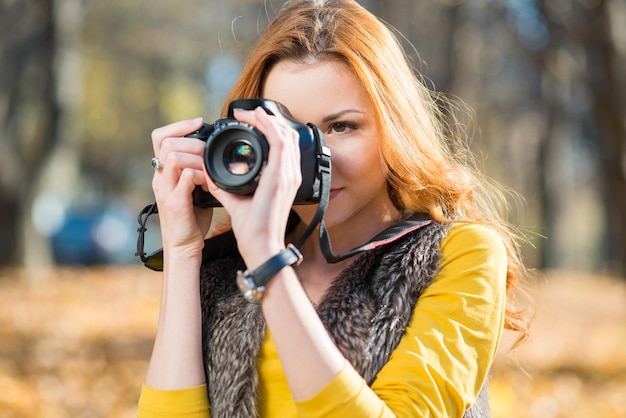 Chica fotógrafa con una cámara hace una sesión de fotos en el parque de otoño