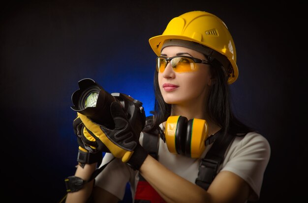 La chica fotógrafa en un sitio de construcción en un casco con una cámara DSLR