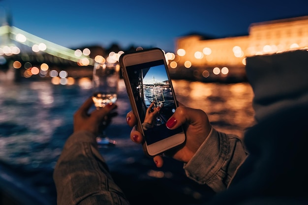 Chica fotografiando por teléfono su mano con un vaso de bebida en th