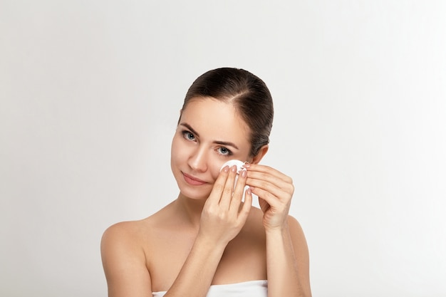 Chica fresca sana quitando el maquillaje de la cara con un algodón