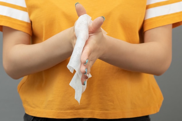 Chica se frota las manos con una toalla sanitaria antibacteriana sobre un fondo gris