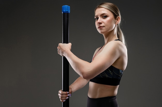 chica fuerte en un top deportivo sostiene un palo de gimnasia y se para a medio lado