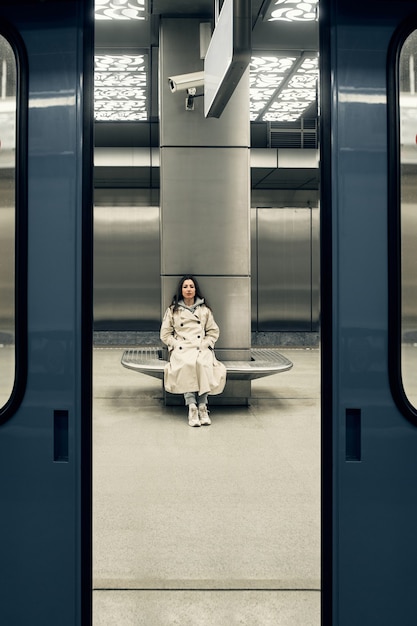 Chica en una gabardina beige en el metro esperando el tren en la plataforma