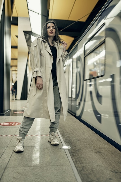 Chica en una gabardina beige en el metro esperando el tren en la plataforma