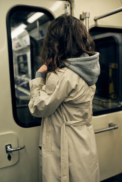 Una chica con una gabardina beige viaja en un vagón de metro.