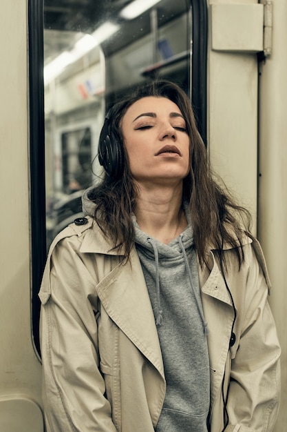 Una chica con una gabardina beige viaja en un vagón de metro.