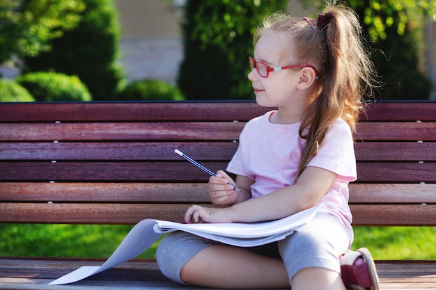 Chica con gafas escribe y dibuja en un cuaderno al aire libre. tarea en la naturaleza.