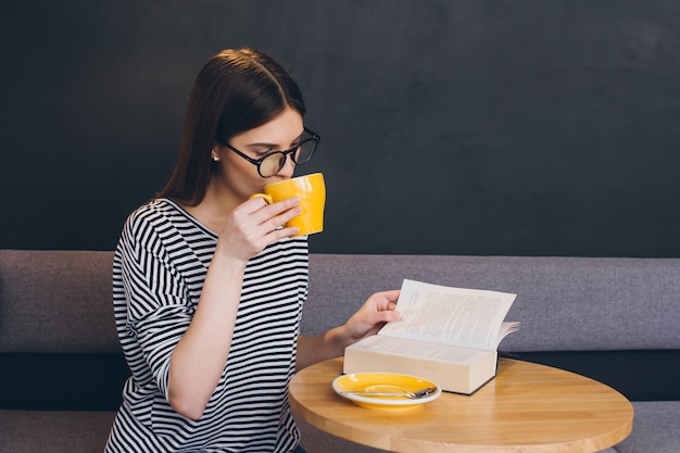 Chica con gafas leyendo un libro en una cafetería.